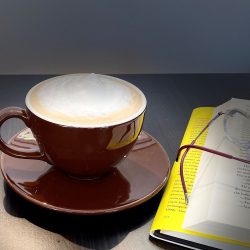 Our signature Cappuccino sitting on a saucer next to a book